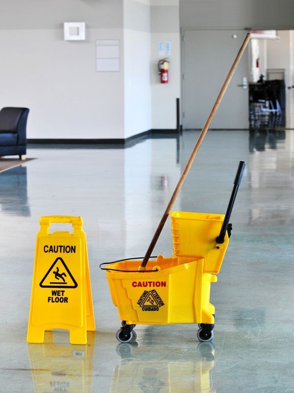 Yellow wet floor sign and cleaning cart with mop, in a hallway.