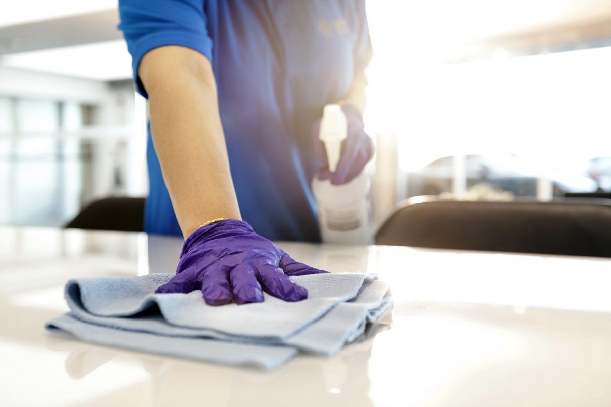 Person in blue shirt and purple gloves wiping a white surface with a blue cloth.