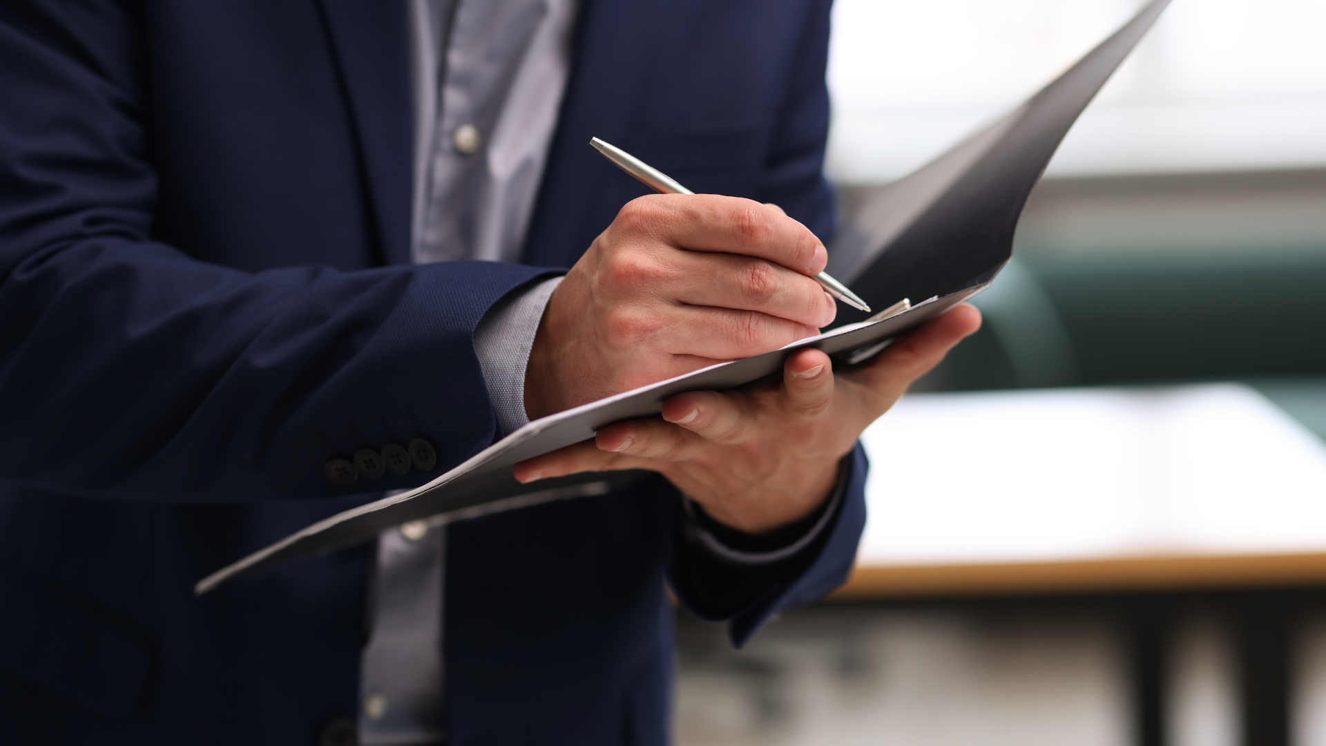Hand holding a stylus over a black tablet in a business setting