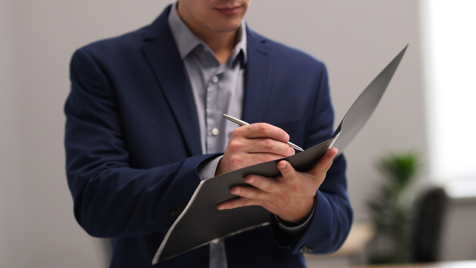 Person in a navy blazer writing on a tablet in a bright office setting