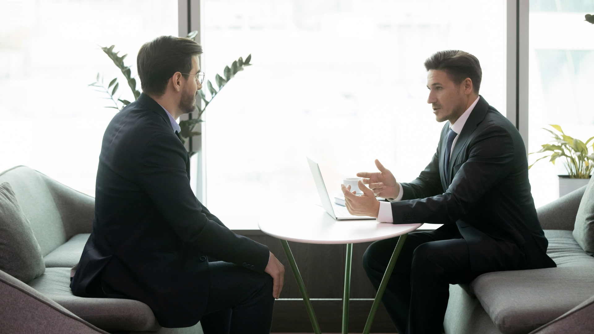 Two businesspeople talking across a small table in a bright office lounge.
