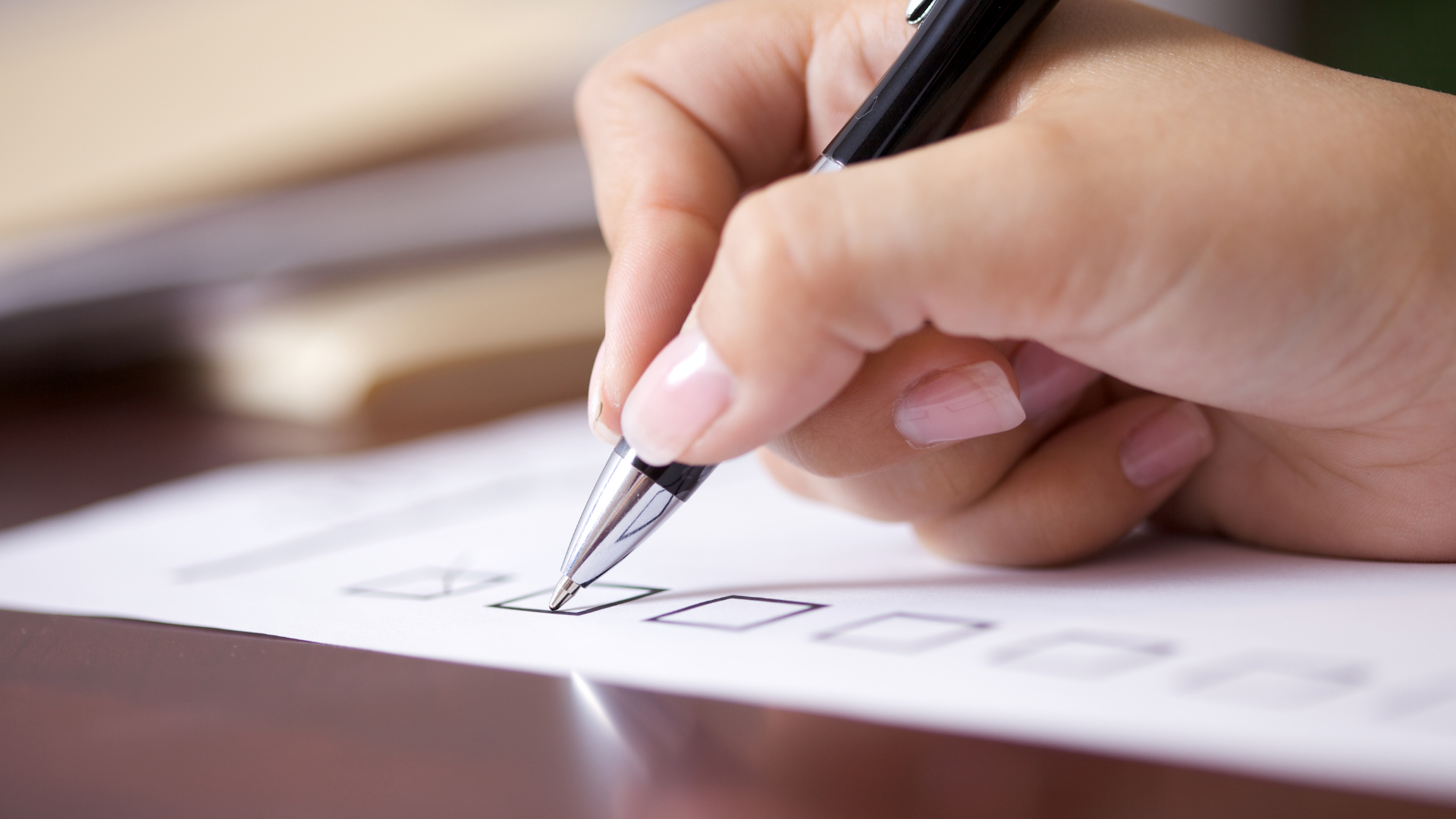Hand writing with a pen on a white sheet of paper at a desk