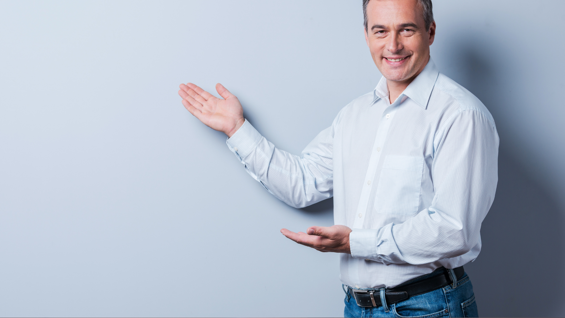 Smiling man in a light blue shirt gesturing toward empty space against a pale background
