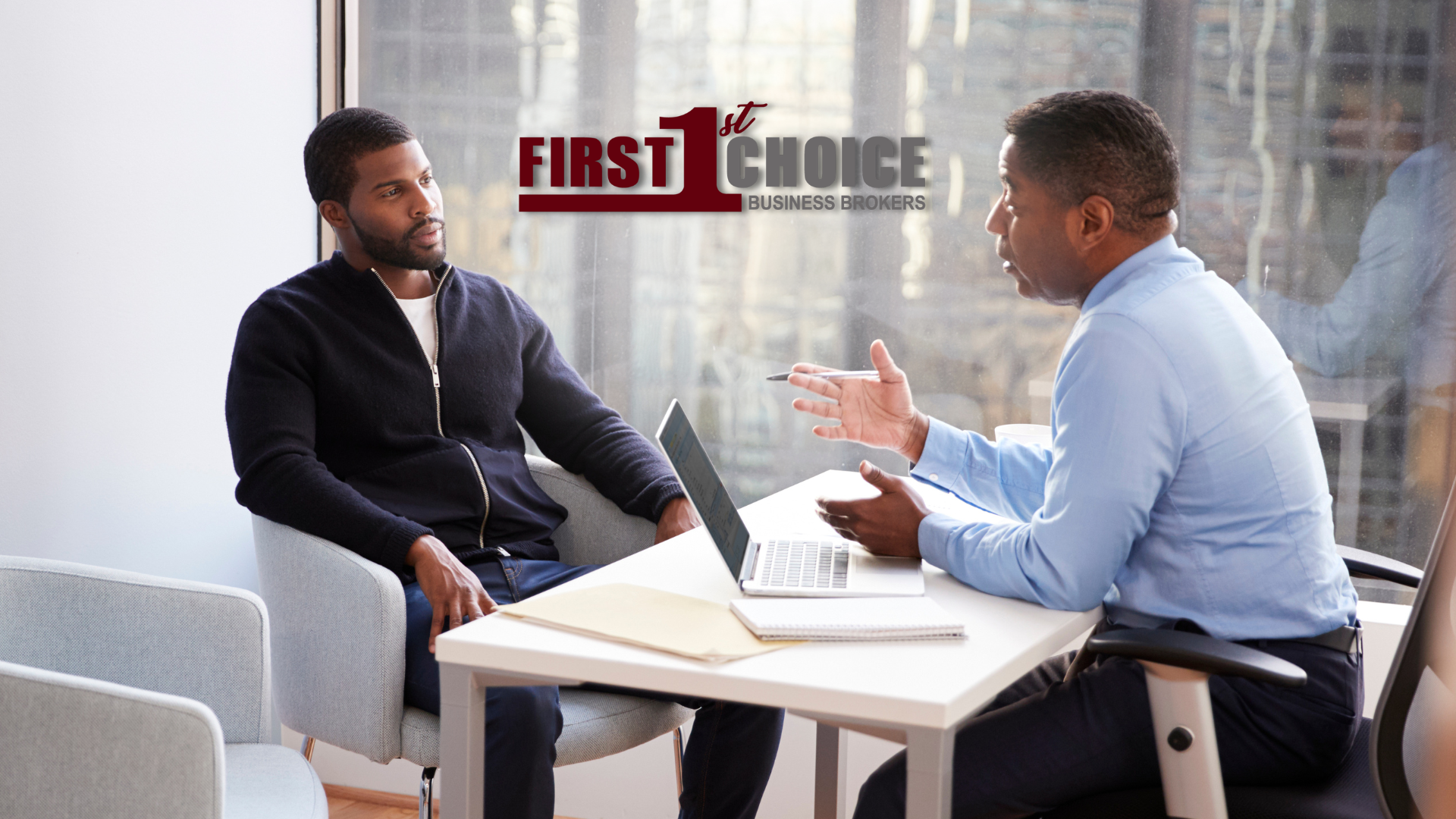 A man is pointing at a tablet while another man looks at a laptop.