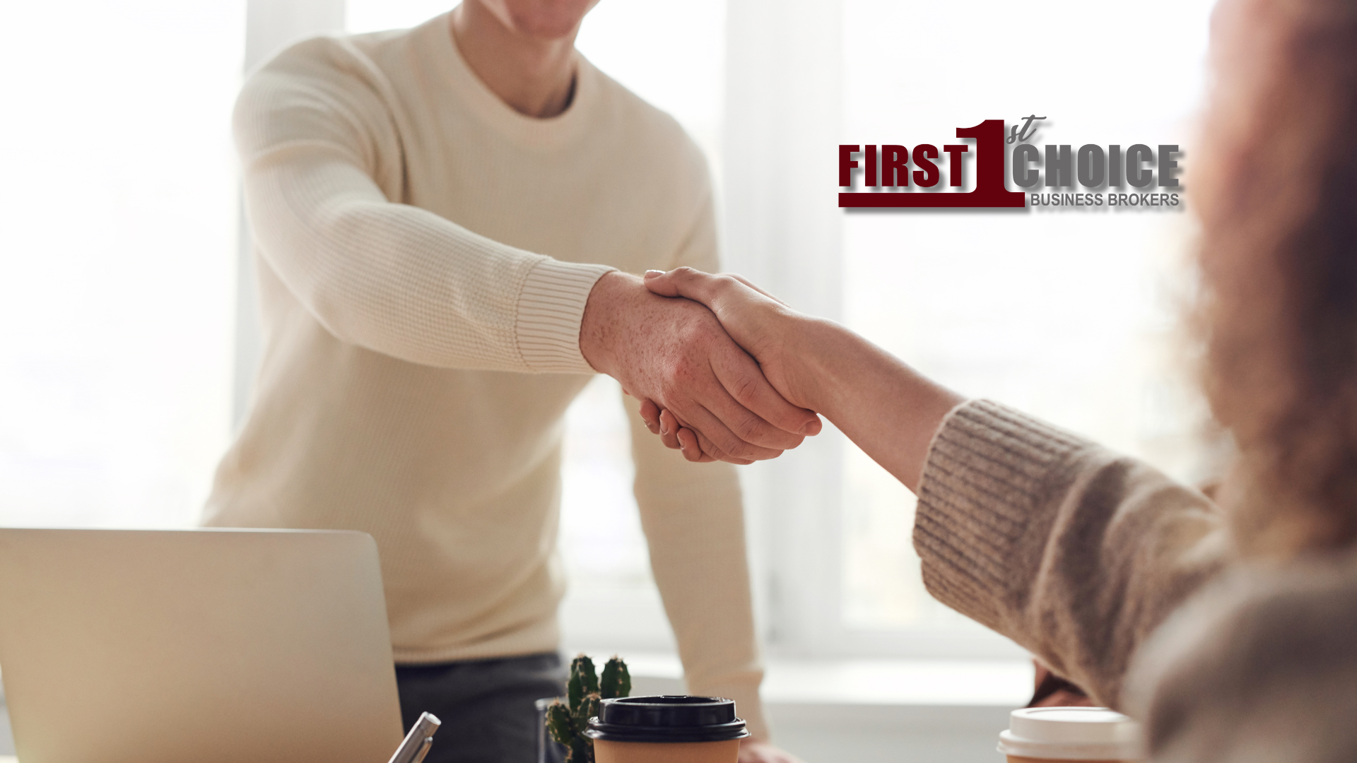 A man and a woman are shaking hands in front of a laptop.