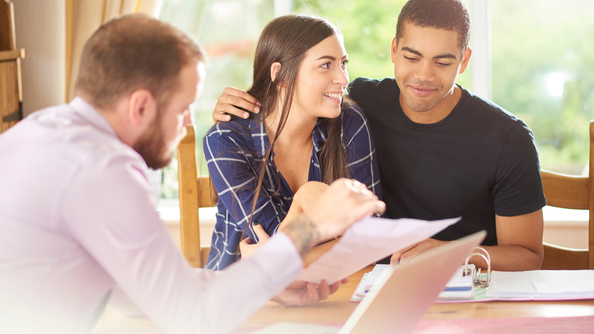 A financial advisor reviews paperwork with a couple at a table, discussing finances in their home.