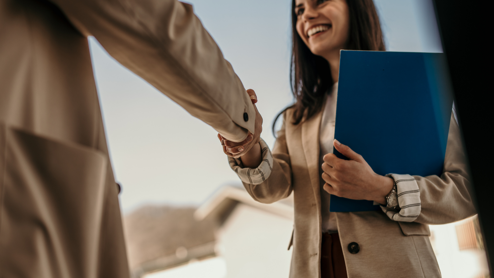 Two people shaking hands, one holding a blue folder, in a bright office setting.