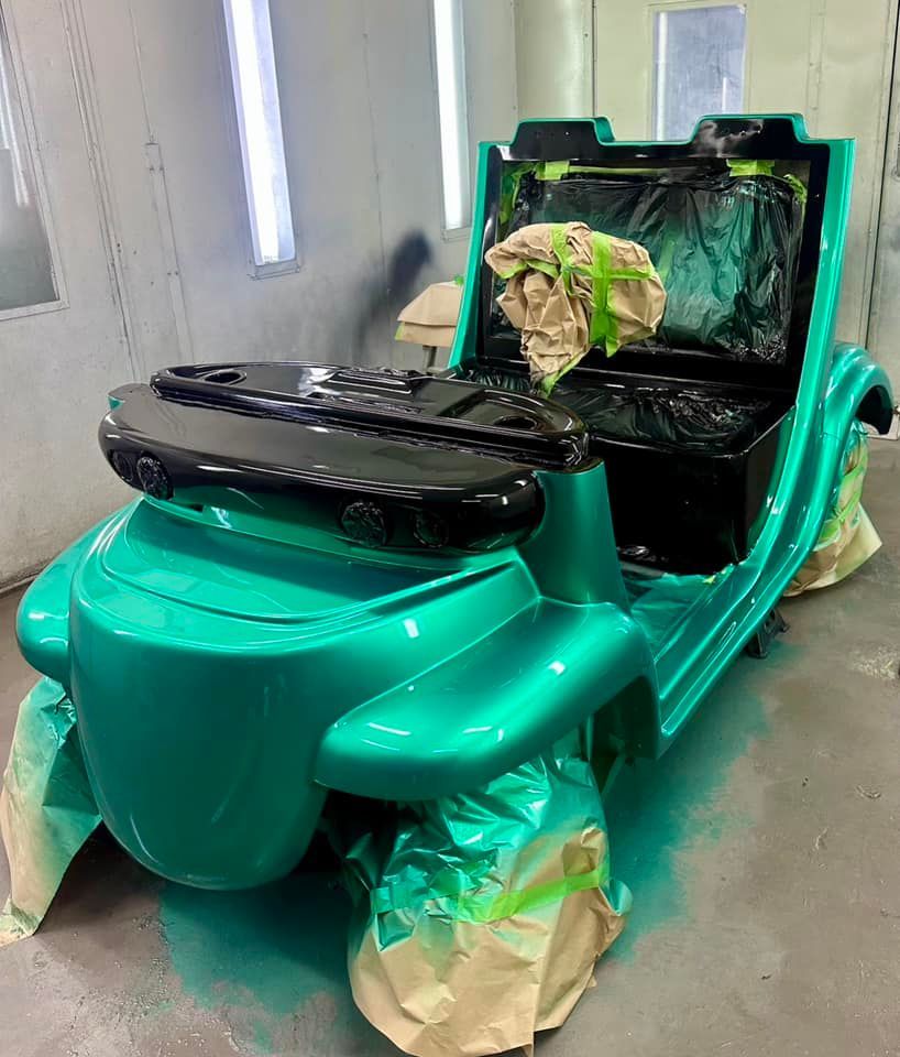 A green golf cart is being painted in a paint booth.