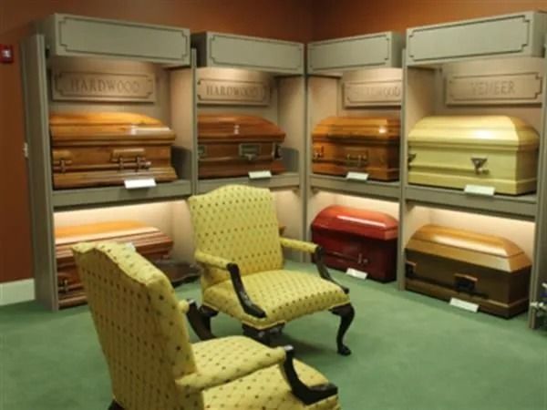 Display of caskets in a funeral home showroom, with two chairs in the foreground.