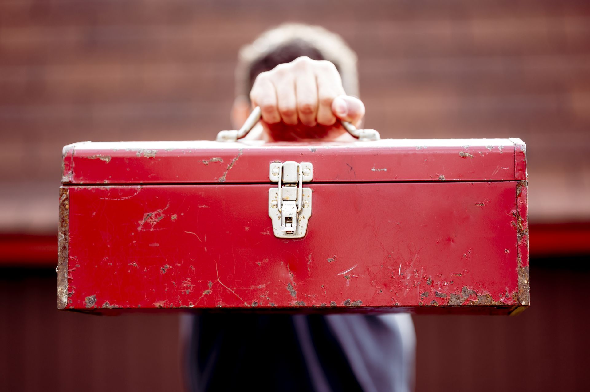 Person holding up a weathered, red toolbox.