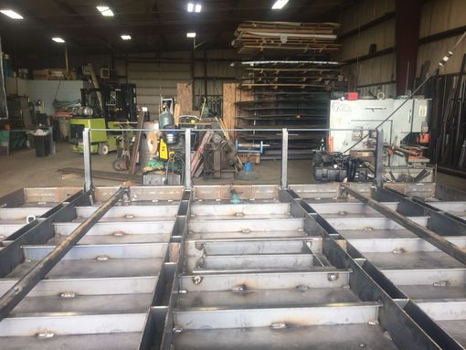 A metal fabrication workshop showing a rectangular steel frame structure being built with vertical support posts.