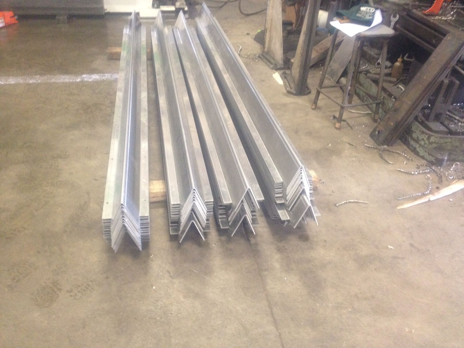 Several long, silver-colored metal angle bars arranged in rows on a concrete shop floor.