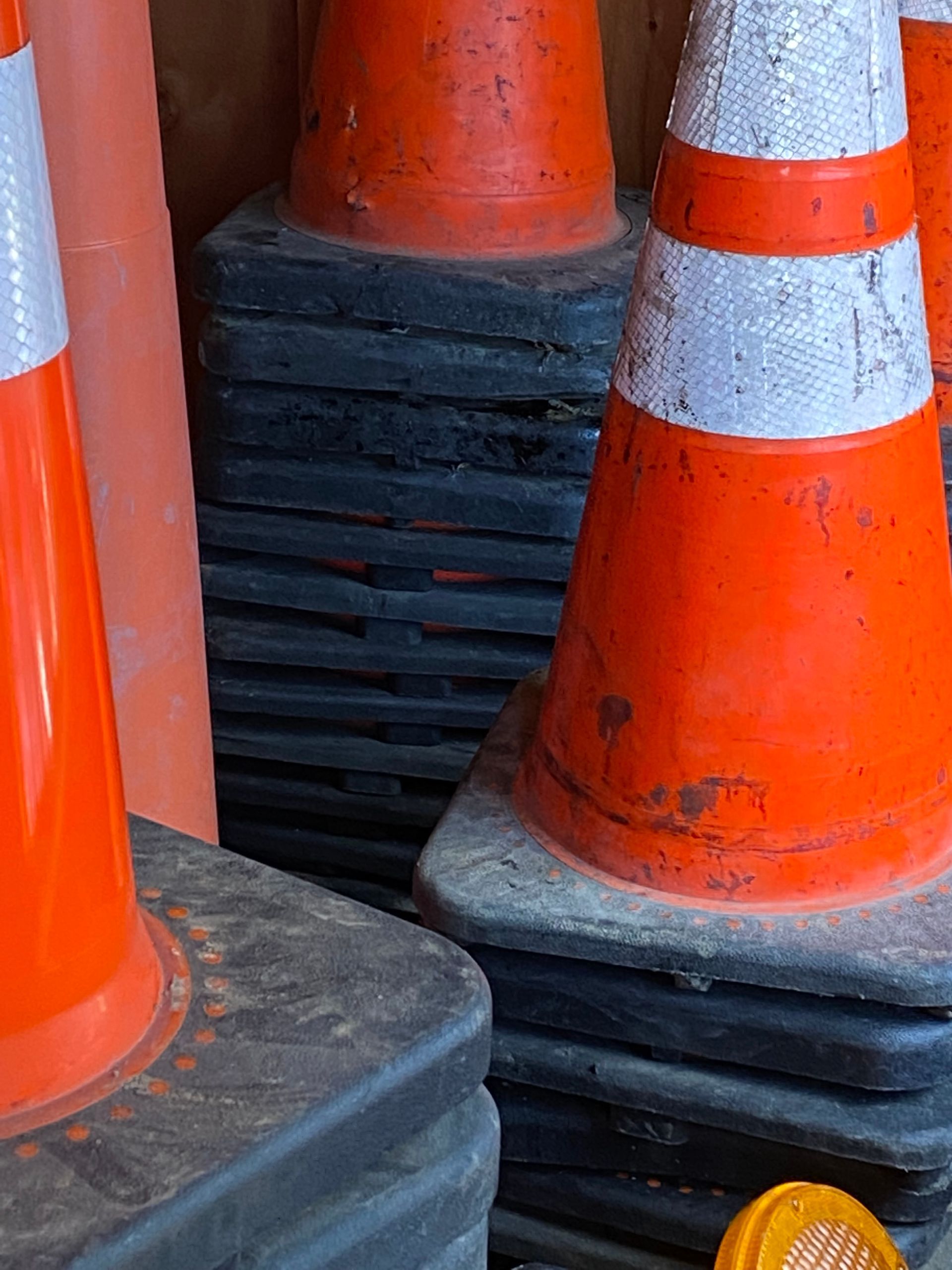 Orange traffic cones stacked together on a black base, with white reflective bands and scuffed surfaces.