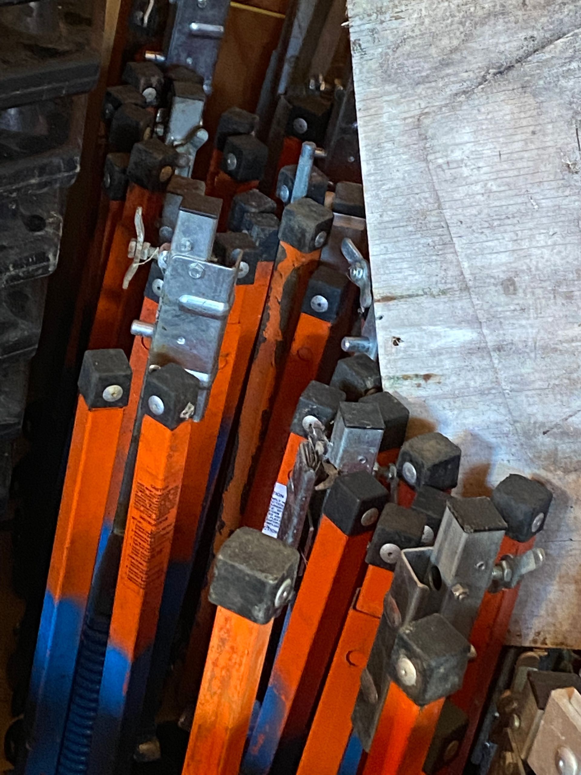 Stacked orange metal clamps with dark bolts and gray parts, stored tightly together.