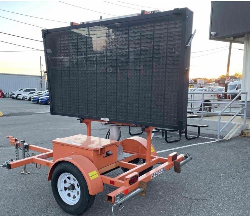 Portable electronic message board on an orange trailer in a parking lot outdoors