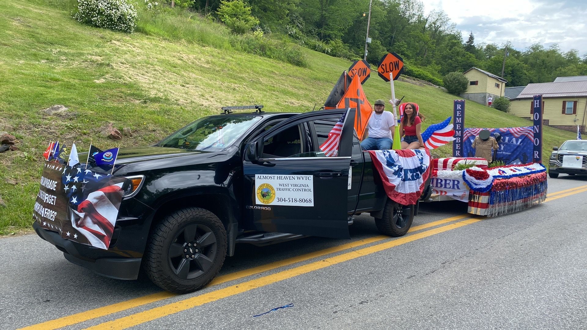 Decorated black pickup truck in a parade with American flags and red, white, and blue bunting on a road.