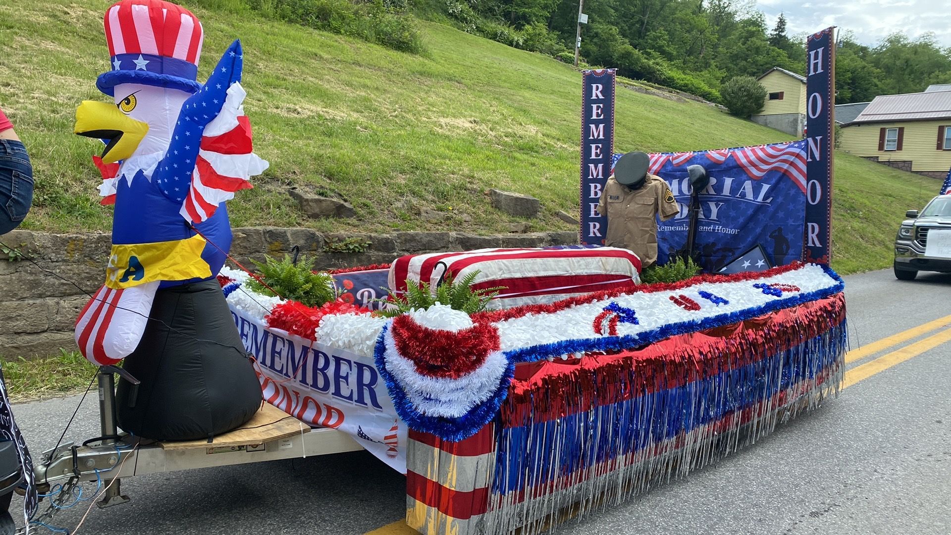 Decorated parade float with red, white, and blue bunting and a bald eagle figure on a road in a green hillside area