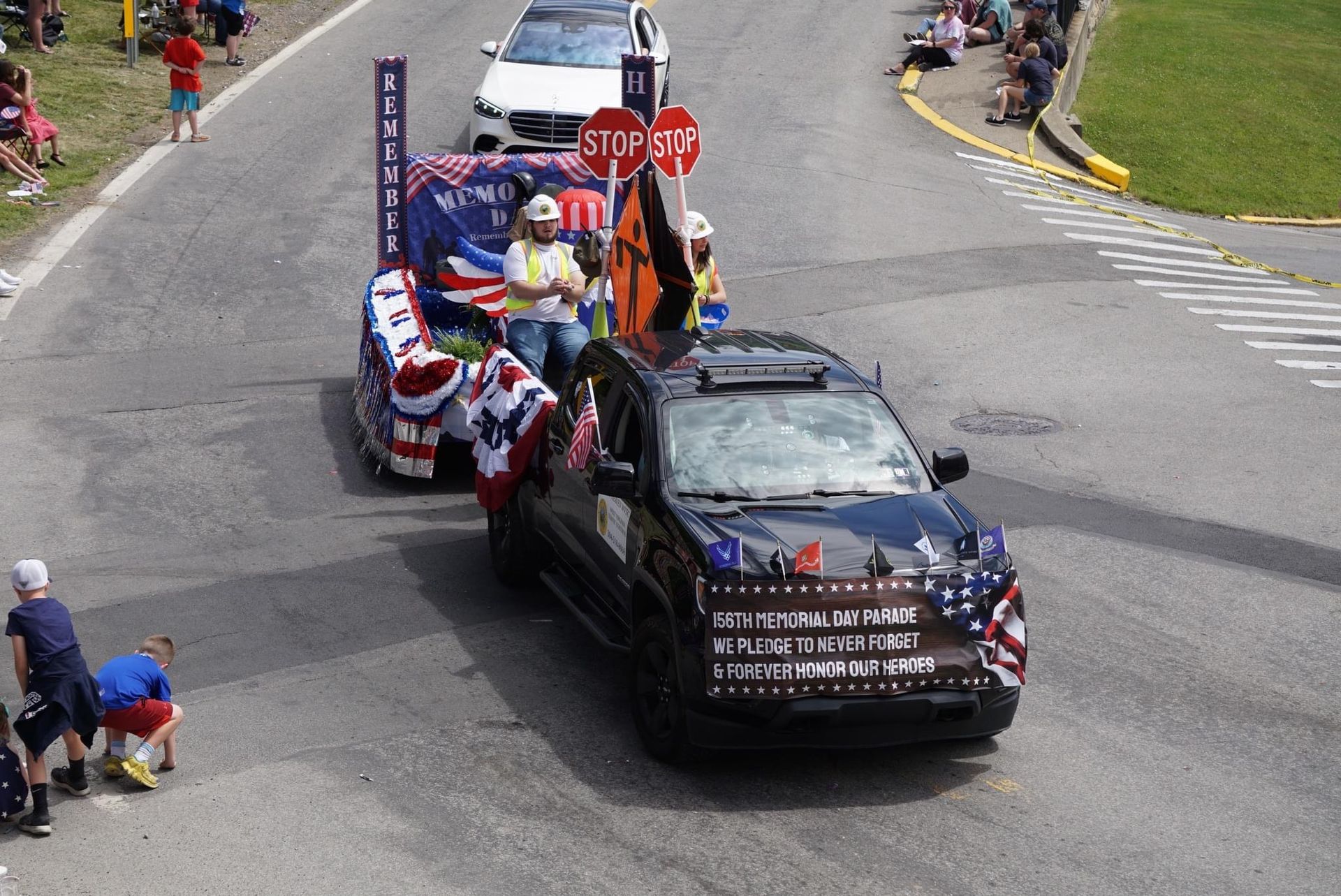 Decorated parade vehicles carrying people around a street corner near a stop sign