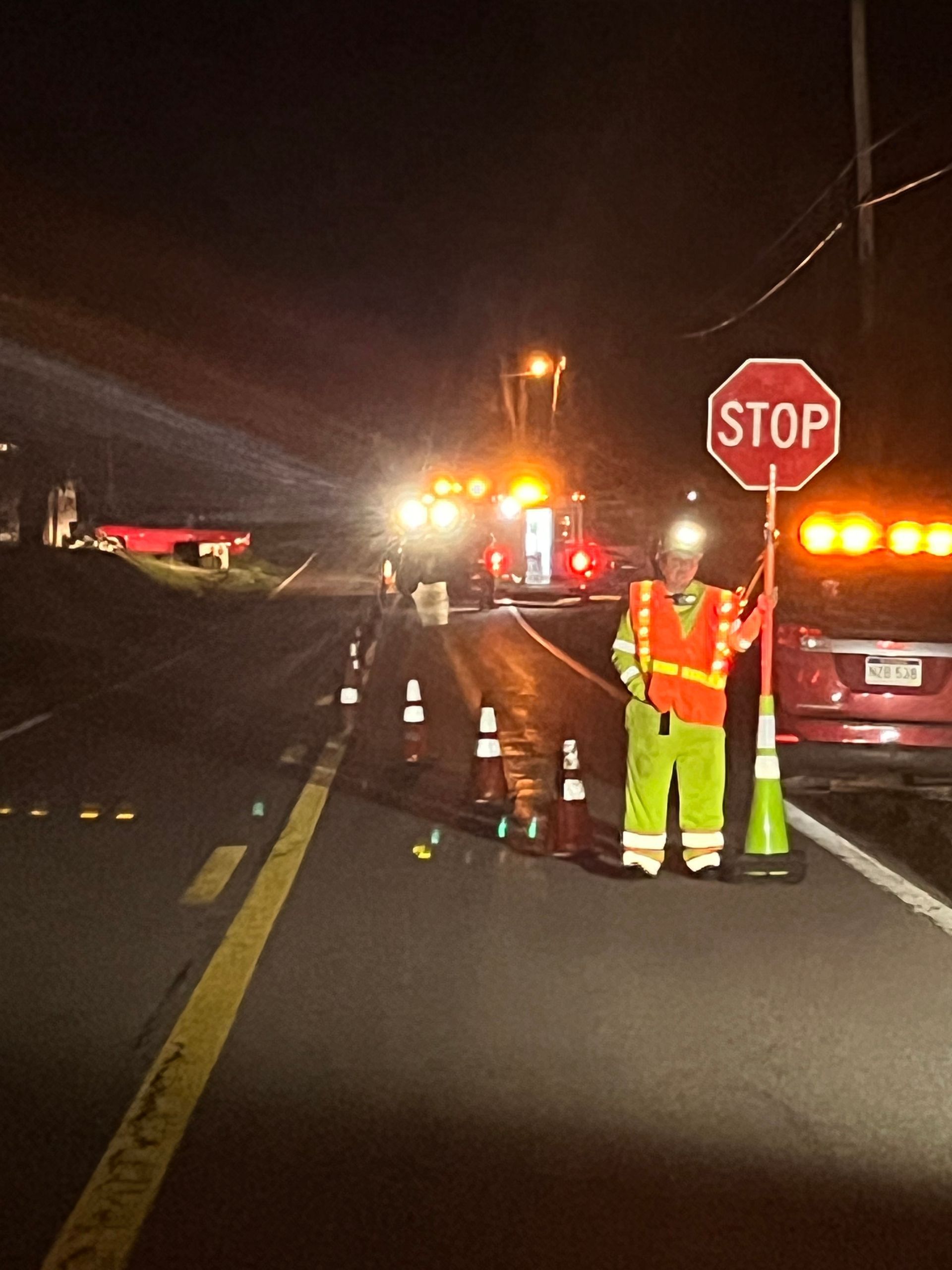 Roadside accident scene at night with emergency vehicles, traffic cones, and a stop sign