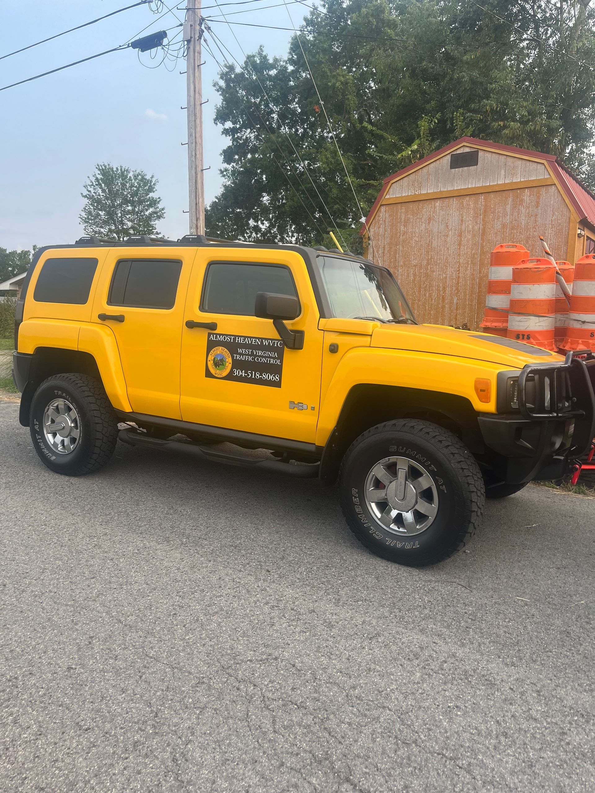 Yellow Hummer SUV parked on a street beside orange traffic barrels and a small shed