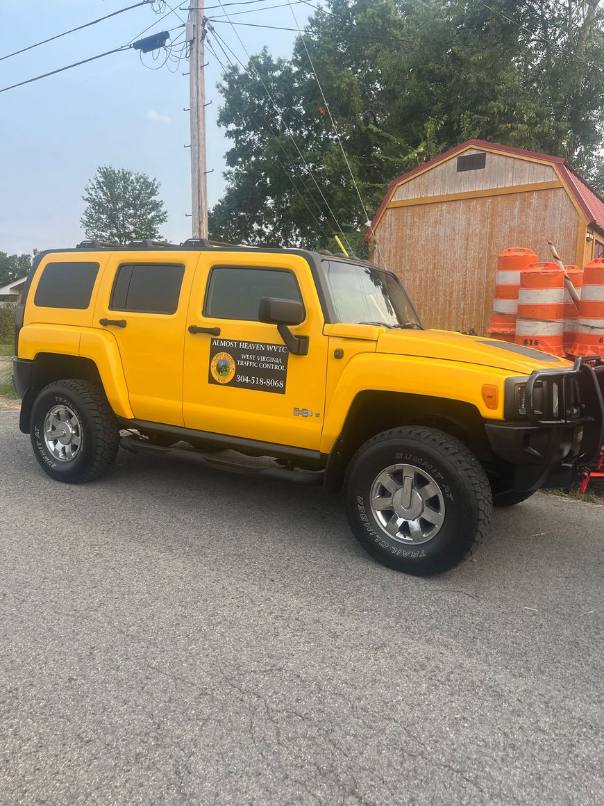 Yellow Hummer SUV parked beside orange traffic barrels and a small shed on a street