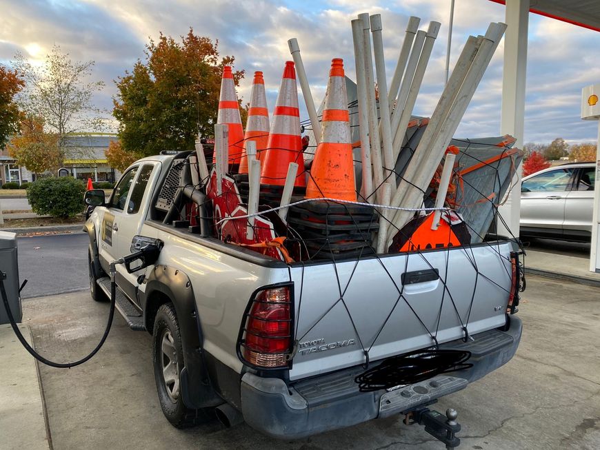 Pickup truck loaded with red poles at a gas station pump at sunset