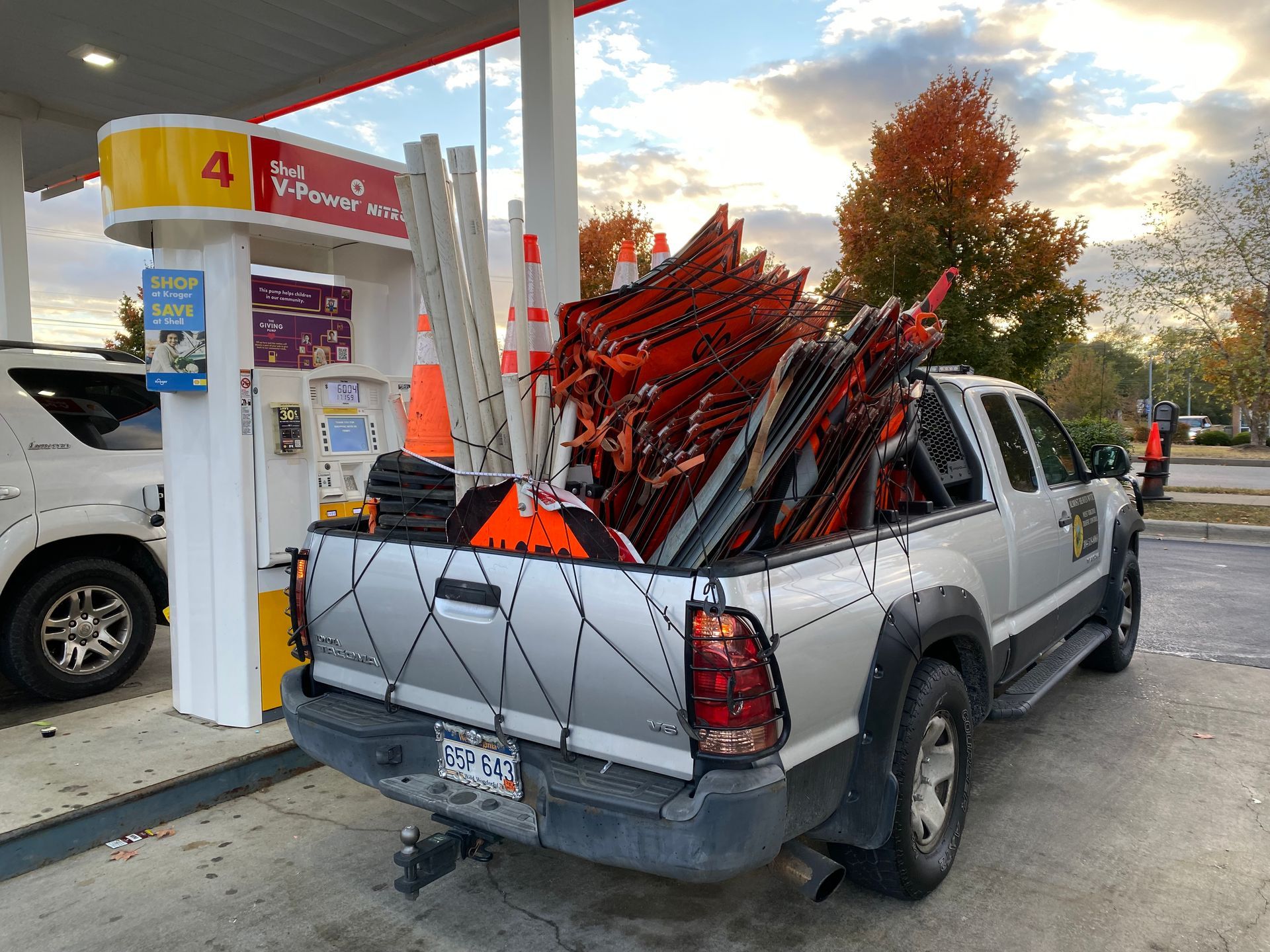 Silver pickup truck loaded with red folding chairs at a gas station pump at sunset