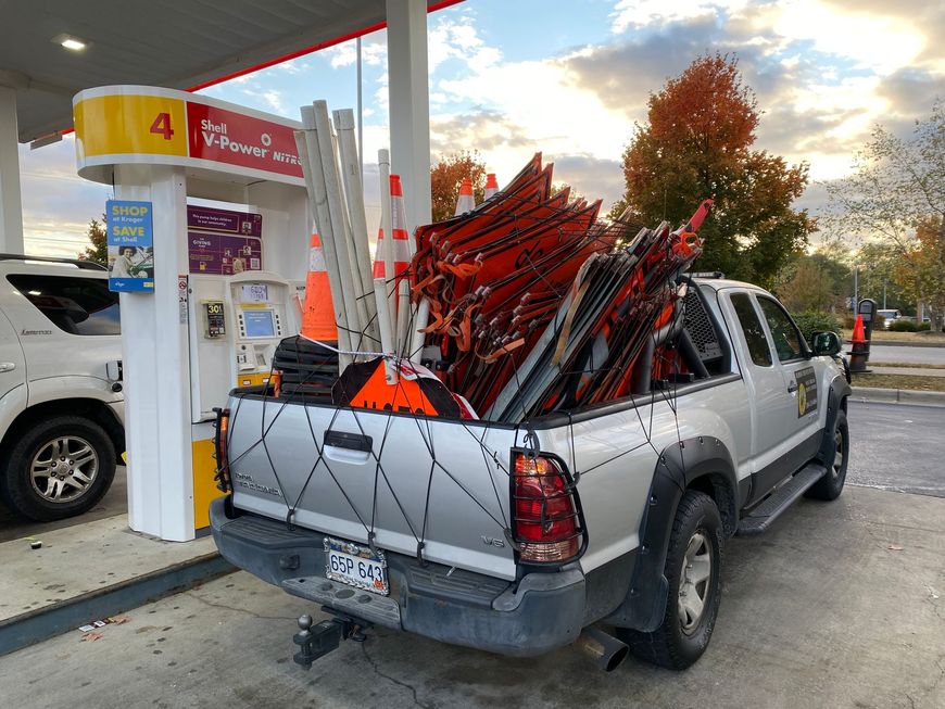 Pickup truck loaded with red and black folded chairs at a gas station pump