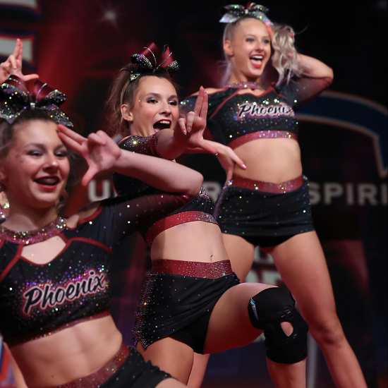 Cheering cheerleaders in black and pink uniforms performing onstage at a competition