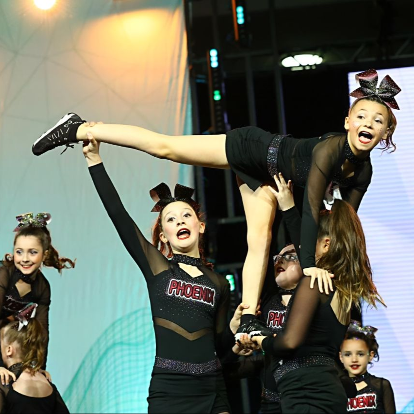 Cheer team performing a lifted stunt on stage, with a smiling flyer held horizontally overhead.