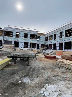 Chantier : immeuble collectif à ossature bois avec revêtement en contreplaqué, fenêtres, sol enneigé et ciel dégagé.
