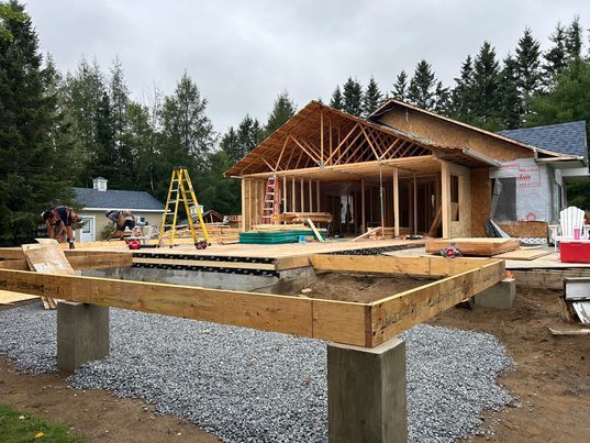 Construction d'une maison avec terrasse. Ossature bois, piliers en béton, sol en gravier.