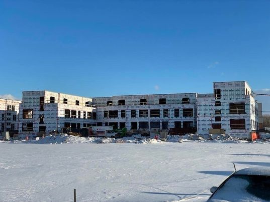 Bâtiment en construction, trois étages, blocs de béton apparents, sol enneigé, ciel bleu clair.