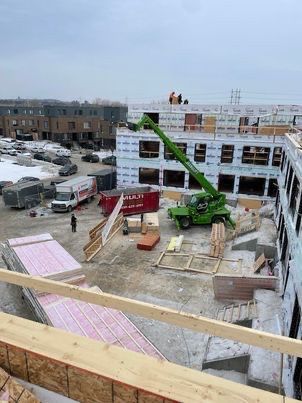 Chantier de construction avec une nacelle élévatrice verte, des ouvriers sur le bâtiment et des matériaux au sol.