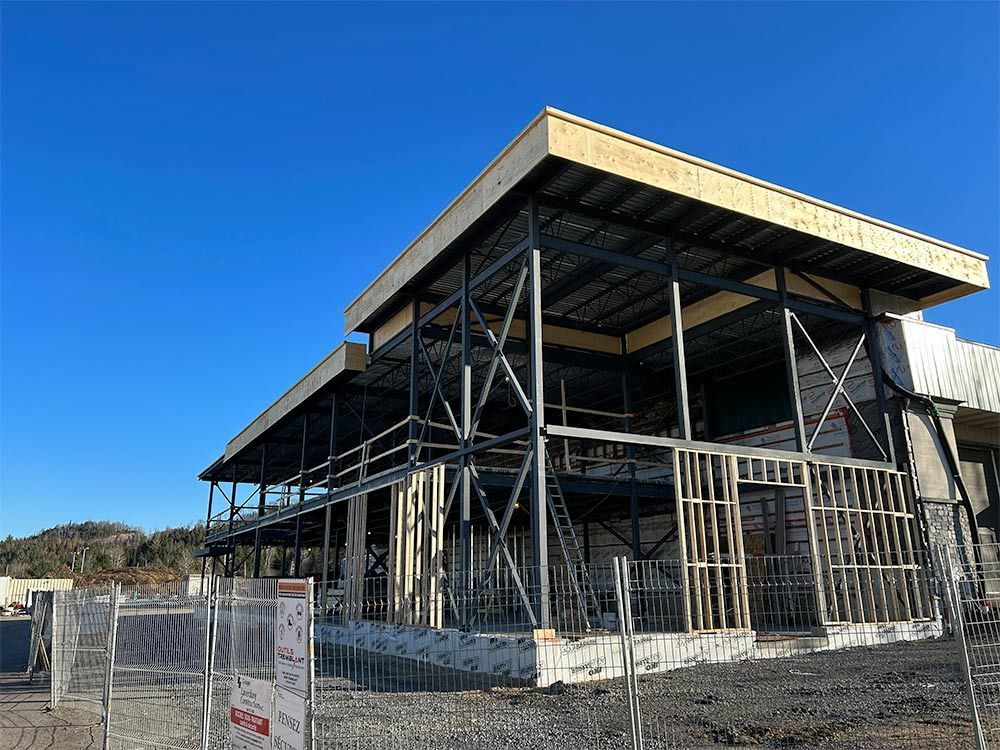 Construction d'un bâtiment à deux étages avec une structure en acier et un toit en bois sous un ciel bleu.