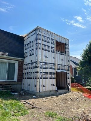 Construction d'une extension de deux étages à une maison en briques. Ossature bois verticale recouverte d'un bardage blanc.