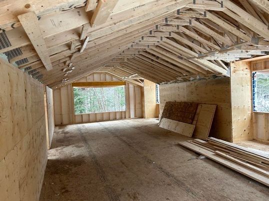 Intérieur d'un bâtiment à ossature bois en construction, avec poutres apparentes et une grande fenêtre.