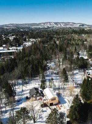 Vue aérienne d'un paysage enneigé avec des bâtiments et une piste de ski visibles au loin.