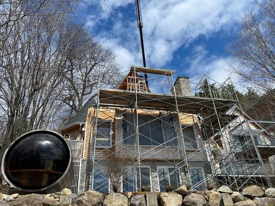 Maison en construction avec échafaudages et grue, ciel bleu visible.
