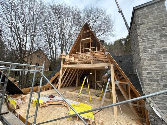 Construction d'une extension de toiture sur une maison. Charpente en bois, échafaudages et outils sont visibles.