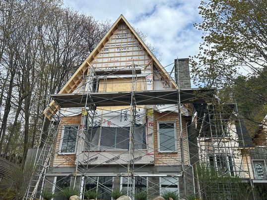Maison en construction avec échafaudages, charpente partiellement apparente et cheminée.