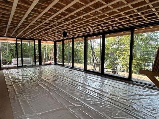 Intérieur d'une pièce avec de grandes fenêtres, un plafond en bois et une bâche en plastique au sol.