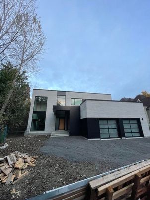 Maison moderne à deux étages en briques claires, avec des touches de noir et un garage double. Ciel couvert.