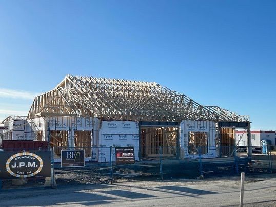 Chantier de construction : maison à ossature bois en construction, charpente apparente, ciel bleu en arrière-plan.