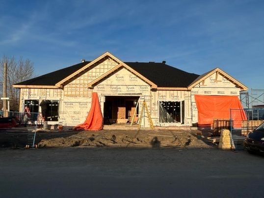 Construction d'un bâtiment d'un étage avec un toit noir et une ossature en bois sous un ciel bleu.