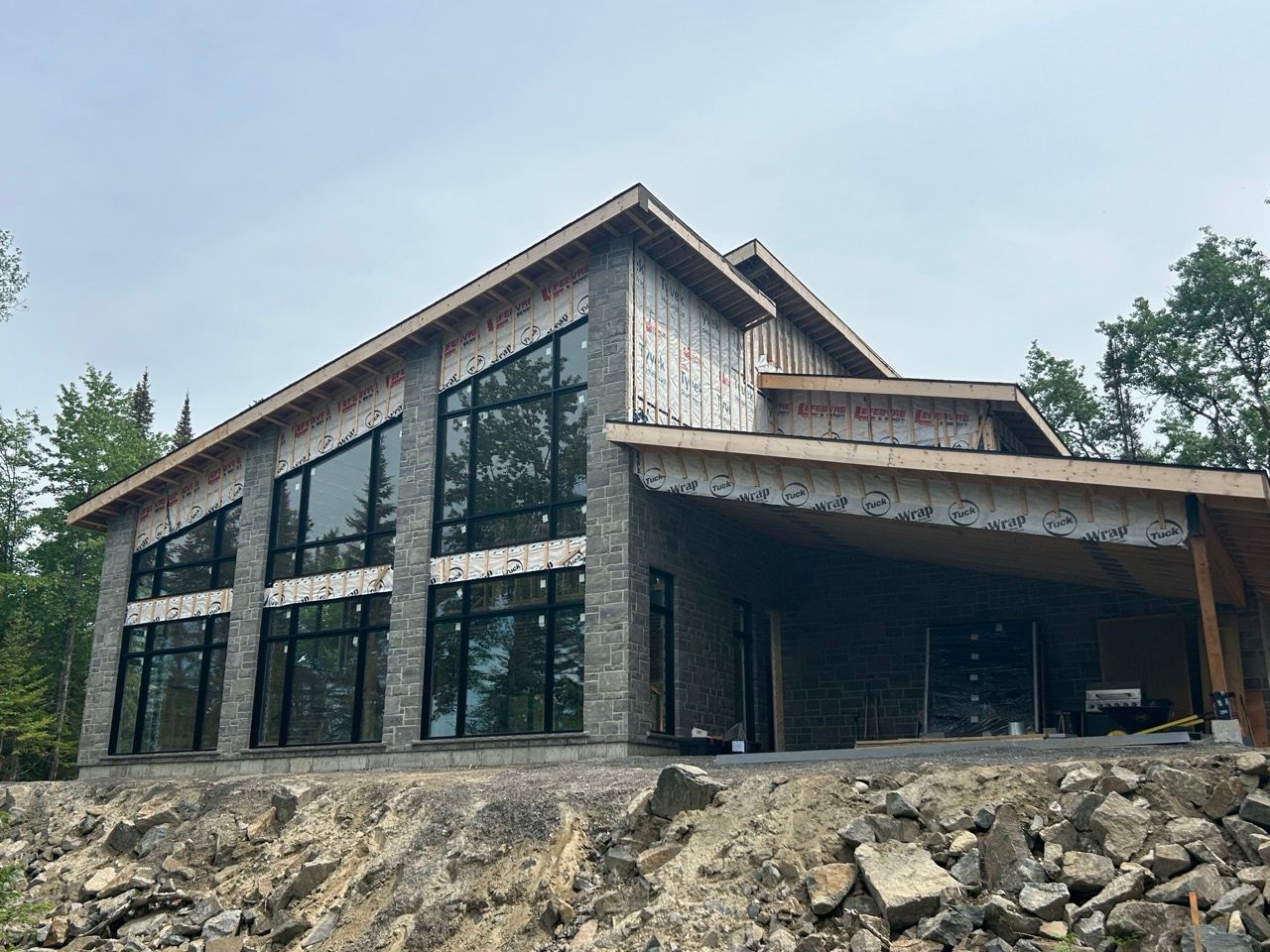 Maison neuve en construction avec revêtement en pierre, grandes fenêtres et porche couvert.