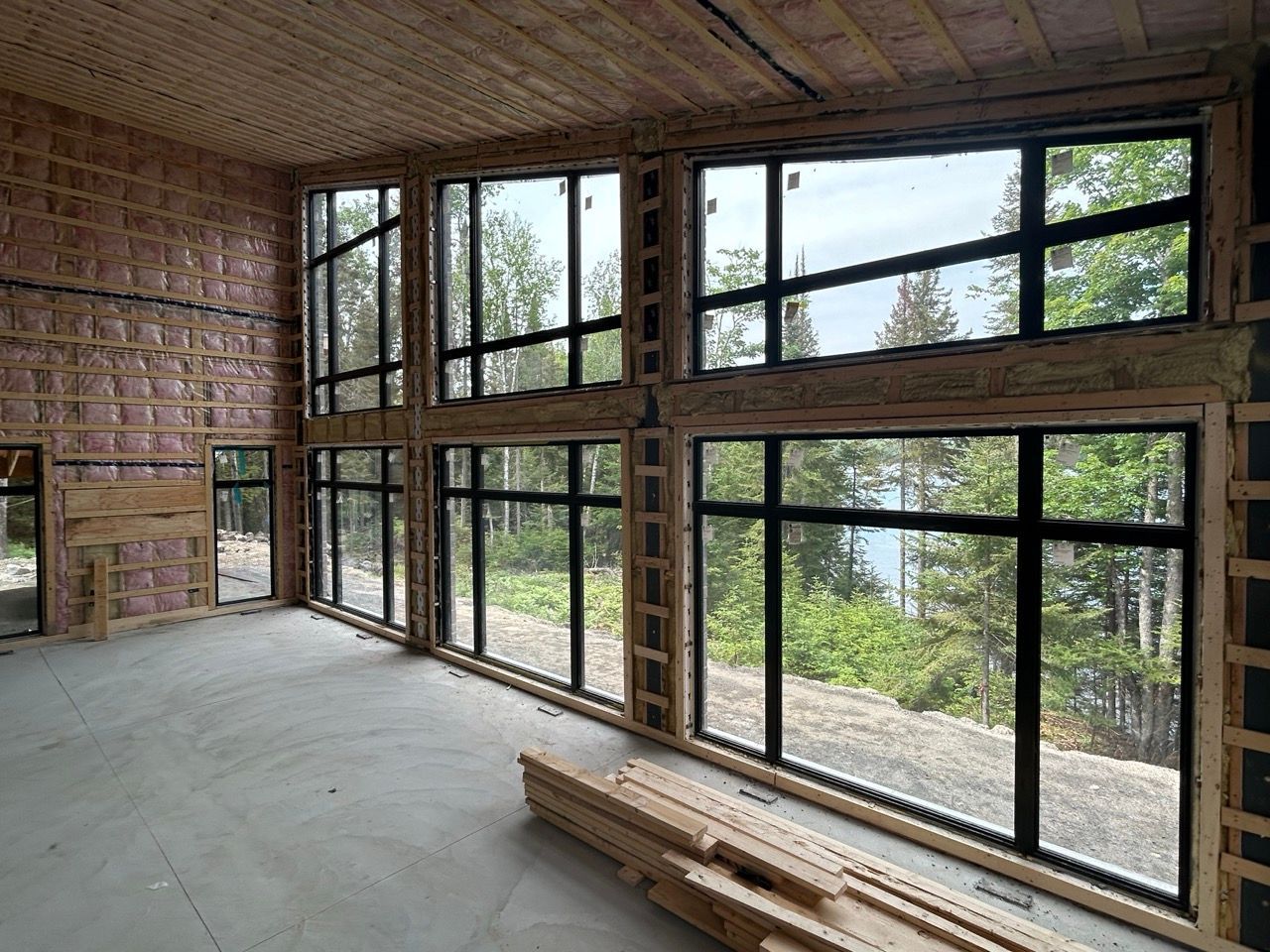 Intérieur d'une maison en construction avec de grandes fenêtres et une vue sur les arbres et l'eau.