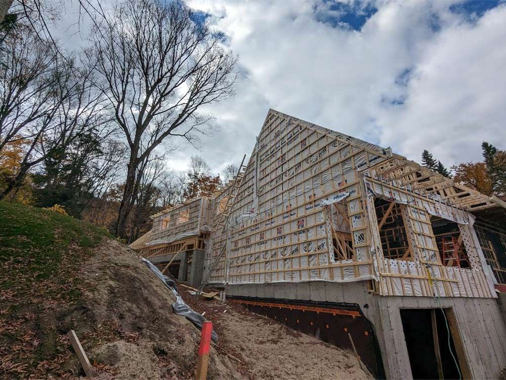Construction d'une maison à flanc de colline, avec charpente et bardage en bois apparents, sous un ciel nuageux.