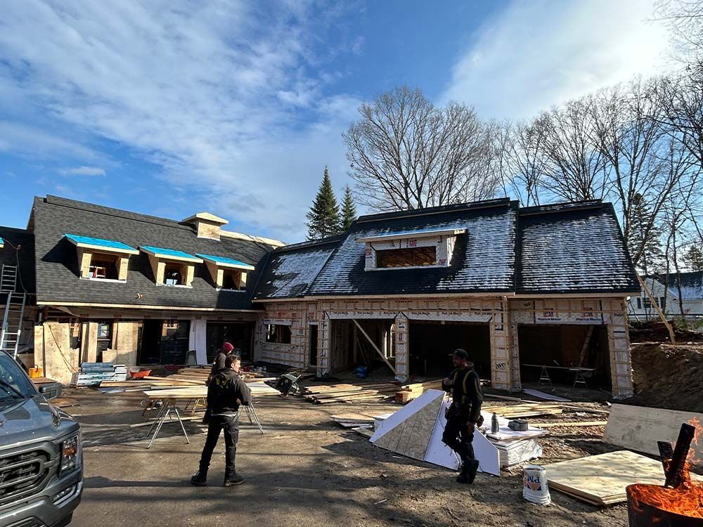 Chantier : structure en bois, partiellement construite, avec deux ouvriers. Ciel bleu, lumière du jour éclatante.
