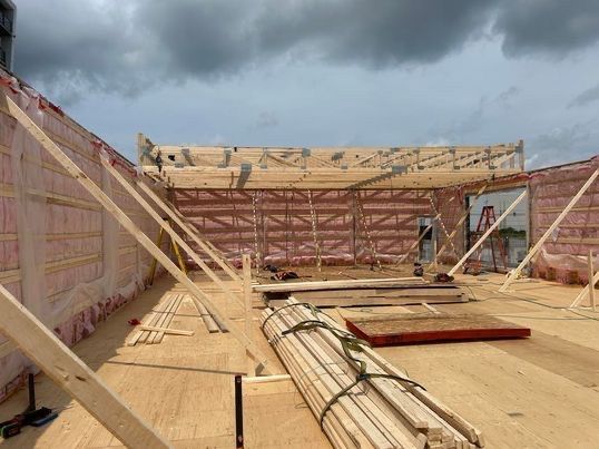 Chantier de construction avec charpente en bois, isolation et bois d'œuvre sur un toit plat sous un ciel nuageux.